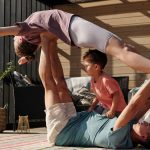 Father and kids doing yoga outdoors on a patio, balancing poses together.